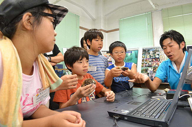 2013年7月20日（土）、公募によって集められた小学生の子供たち20名が参加したミキモトの「真珠の学校」が開校！磯での生物採集や海、真珠についてのレクチャー、そして真珠を育むアコヤ貝への「核入れ」を体験！子供たちからはたくさんの笑顔と真剣な顔が見られました！